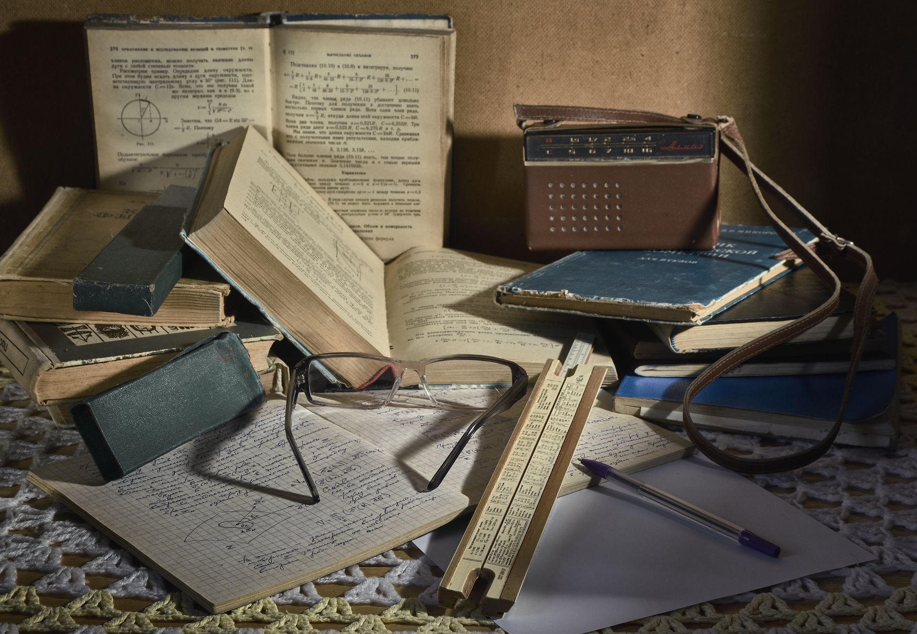Still life of a classic study setting with vintage books, glasses, slide rule, and an old analog radio.