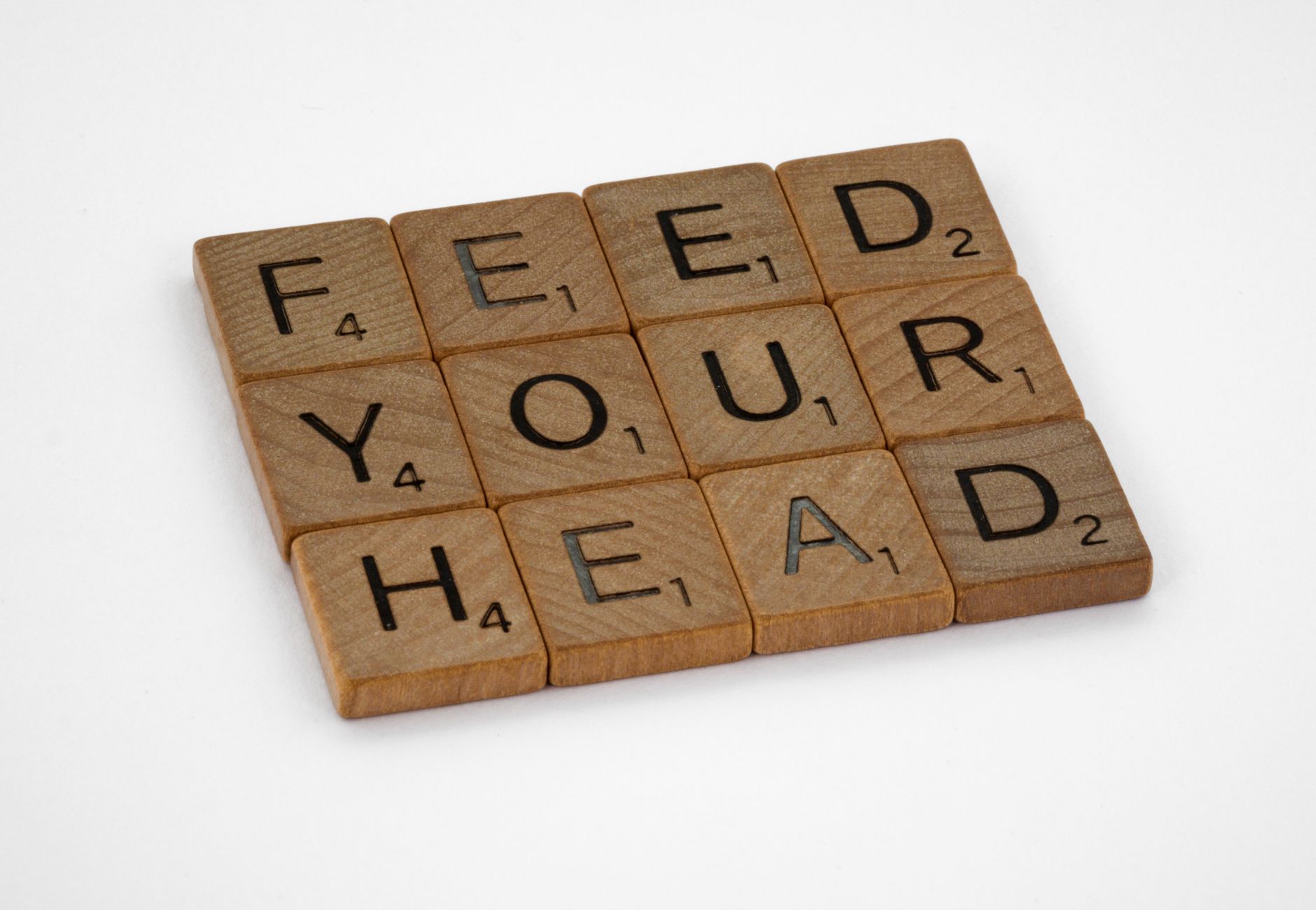 Wooden letter tiles on white surface spelling 'Feed Your Head' from a high angle view.