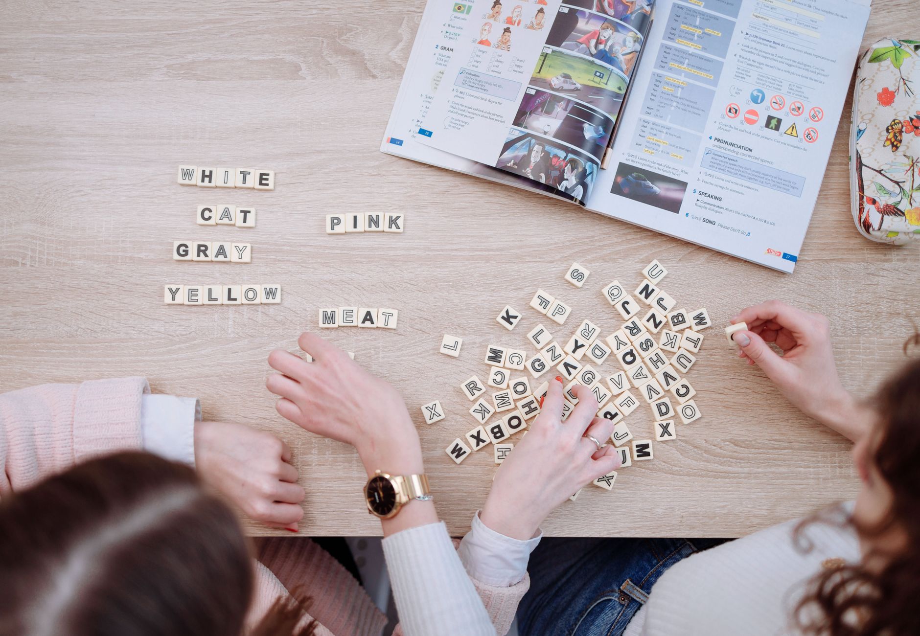 Friends studying together using Scrabble tiles and books, fostering collaborative learning in a casual setting.