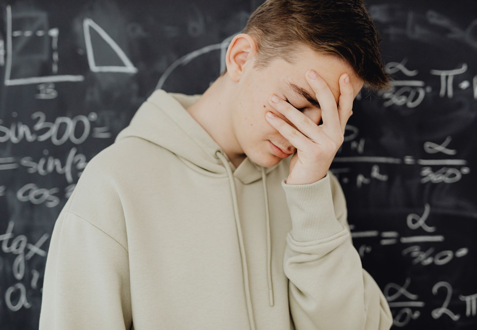 Young man overwhelmed by mathematical calculations on a blackboard in a classroom setting.