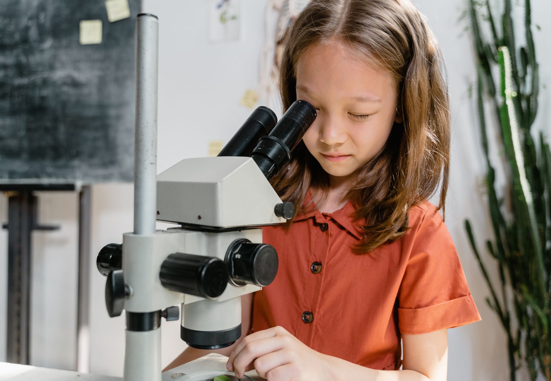 A curious girl examining a sample using a microscope in a classroom setting, focused on learning science.