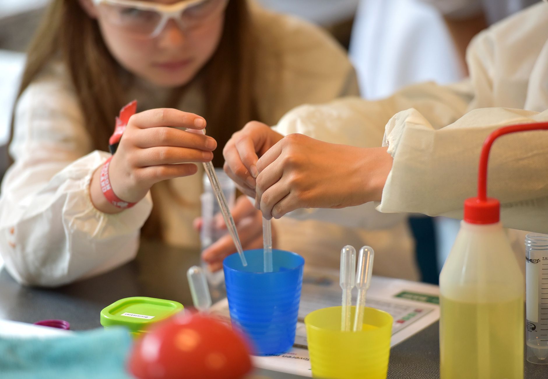 Children conducting science experiments with pipettes and safety glasses in a lab setting.
