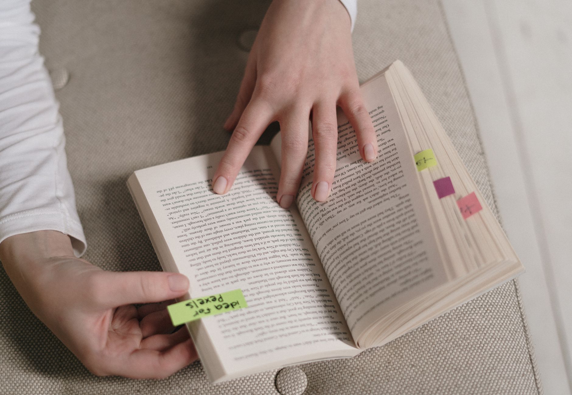 An up-close view of hands holding an open book with colorful bookmarks, ideal for literary themes.